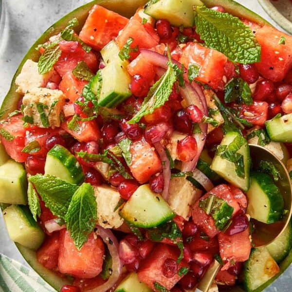 Top down view of watermelon feta salad with cucumber, red onion, and mint served inside a watermelon bowl with a serving spoon.