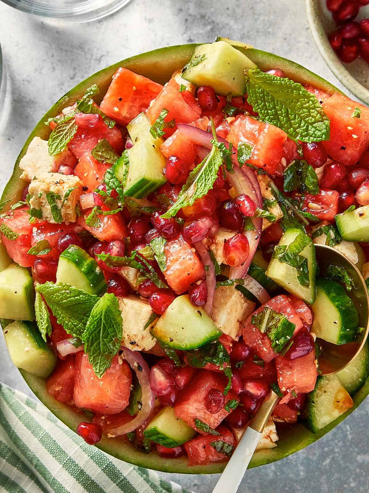 Top down view of watermelon feta salad with cucumber, red onion, and mint served inside a watermelon bowl with a serving spoon.
