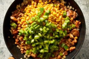 adding capsicum, corn, and jalapeño to the pan with chicken