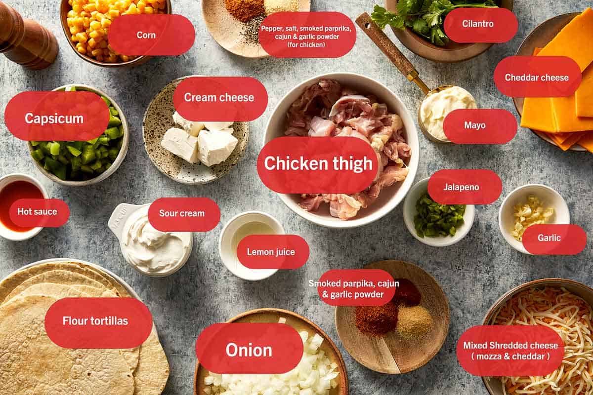Overhead view of raw ingredients for a chicken burrito recipe arranged in small bowls, including diced chicken thighs, flour tortillas, shredded cheese, cream cheese, corn, chopped capsicum, and various spices.