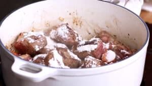 adding the flour to the pan with veggies and beef