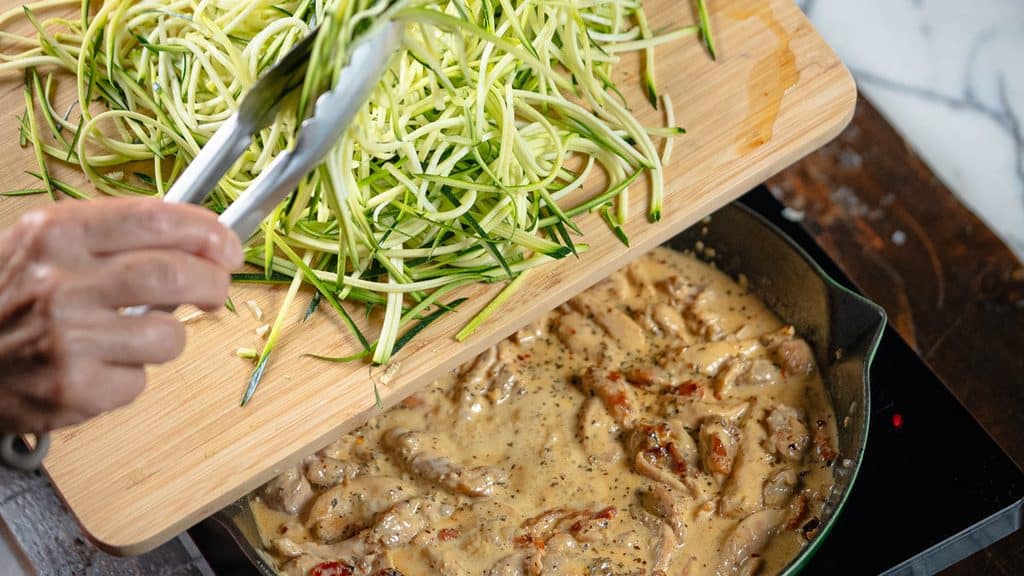 adding the zoodles to the pan with the sauce