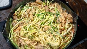 mixing the zoodles in a pan with the chicken and sauce