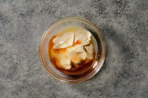 A glass bowl containing mayonnaise, garlic, and hot honey ready to be mixed into a smash burger sauce.