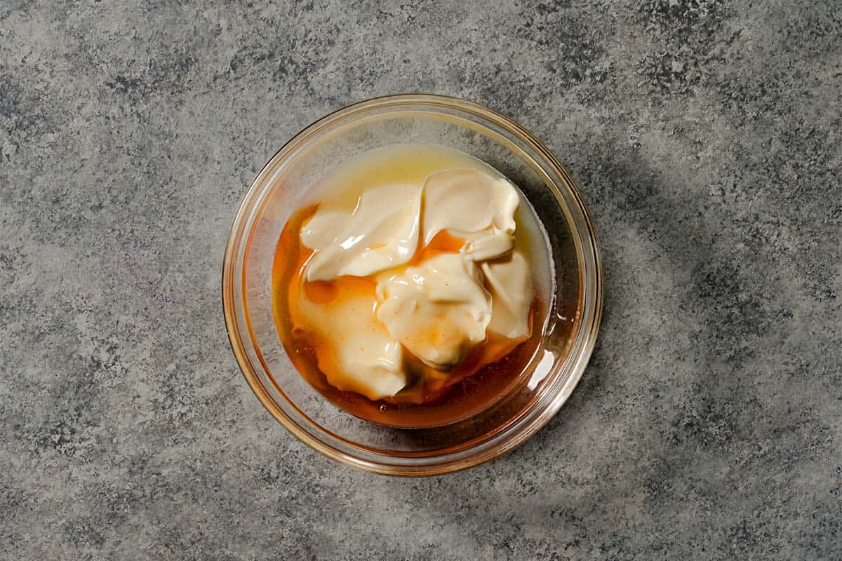 A glass bowl containing mayonnaise, garlic, and hot honey ready to be mixed into a smash burger sauce.