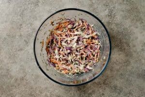 A glass bowl of shredded red and green cabbage mixed with carrots and yogurt dressing to serve with healthy turkey burgers.