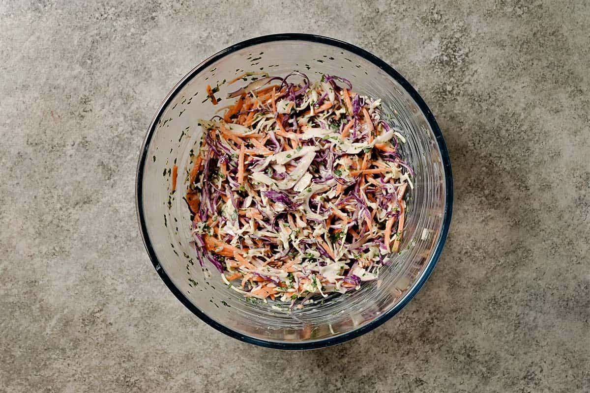 A glass bowl of shredded red and green cabbage mixed with carrots and yogurt dressing to serve with healthy turkey burgers.