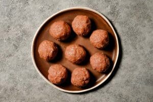 Eight raw seasoned turkey meat balls arranged on a brown plate, ready to be pressed into flat hamburger patties.