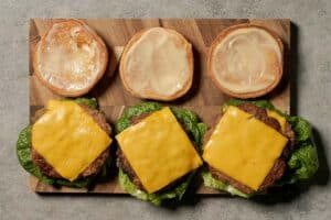 Hands wearing black gloves use a spatula to stack two cooked patties topped with melted cheese in a hot skillet while making turkey smash burgers.