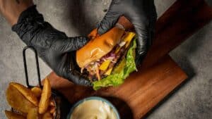 Hands wearing black gloves holding an assembled turkey burger with a bowl of hot honey aioli in the background, showcasing the final result a smash burger recipe.