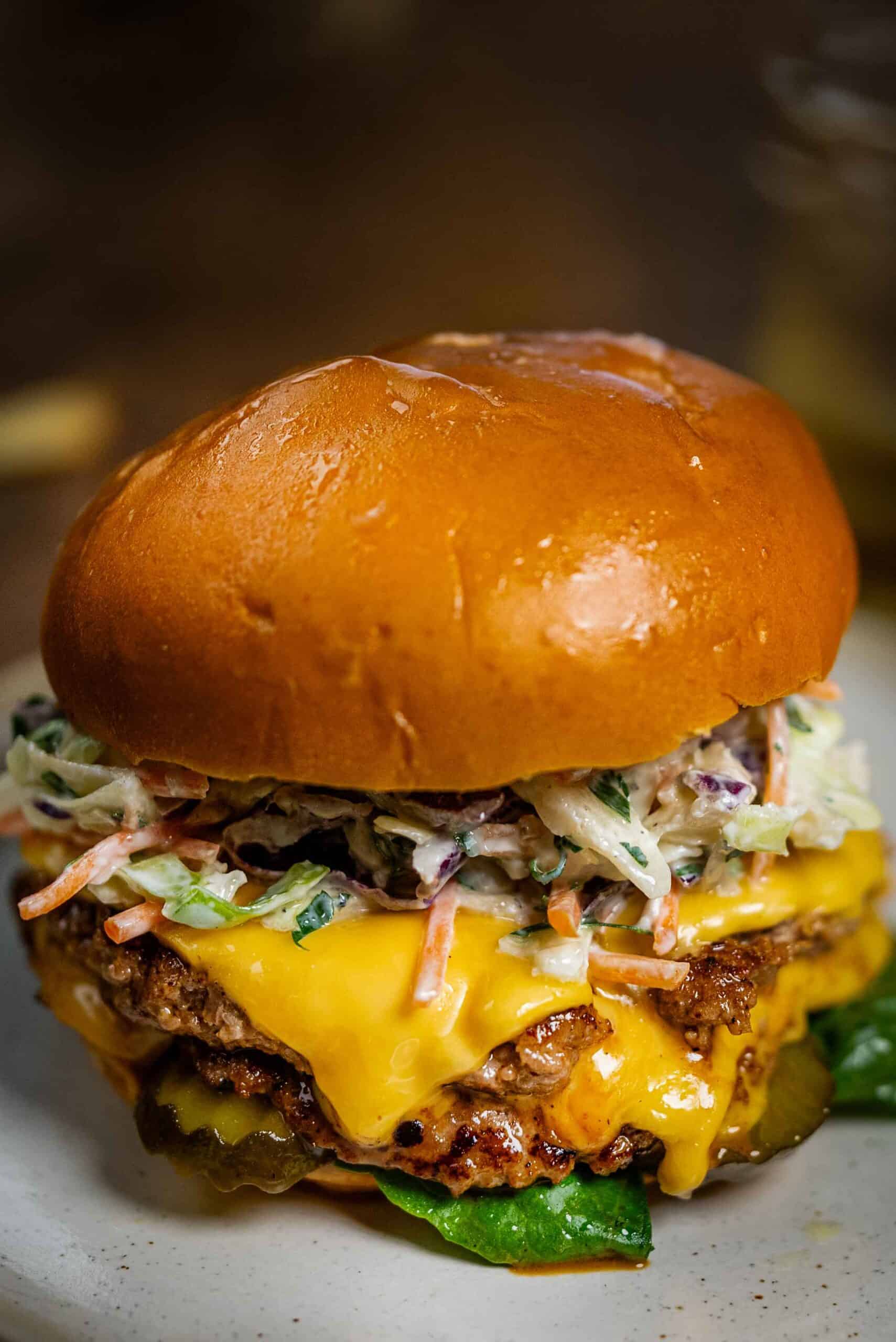 A close-up of a stacked turkey smash burger on a toasted brioche bun, featuring double patties with melted cheddar cheese, creamy coleslaw, sliced pickles, and lettuce.