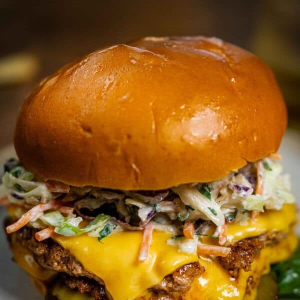 A close-up of a stacked turkey smash burger on a toasted brioche bun, featuring double patties with melted cheddar cheese, creamy coleslaw, sliced pickles, and lettuce.