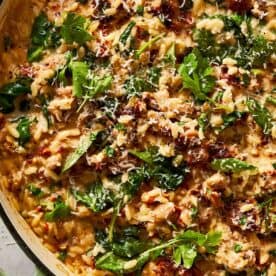 Close-up of creamy Italian sausage and spinach orzo in a skillet, garnished with Parmesan and parsley.