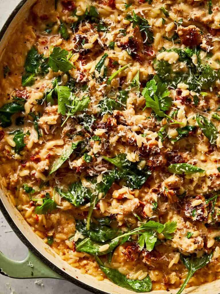 Close-up of creamy Italian sausage and spinach orzo in a skillet, garnished with Parmesan and parsley.
