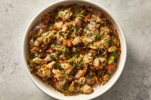 Fully mixed raw shrimp dumpling filling in a bowl, showing the chopped prawns, shredded carrots, spinach, and seasonings combined into a cohesive mixture.