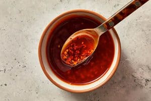 A small bowl of dark red dumpling sauce with a spoon resting inside, lifting some of the chili flakes from the mixture.