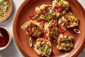 Fully cooked shrimp dumplings served on a plate, heavily drizzled with chili sauce and garnished with sliced green onions and sesame seeds.