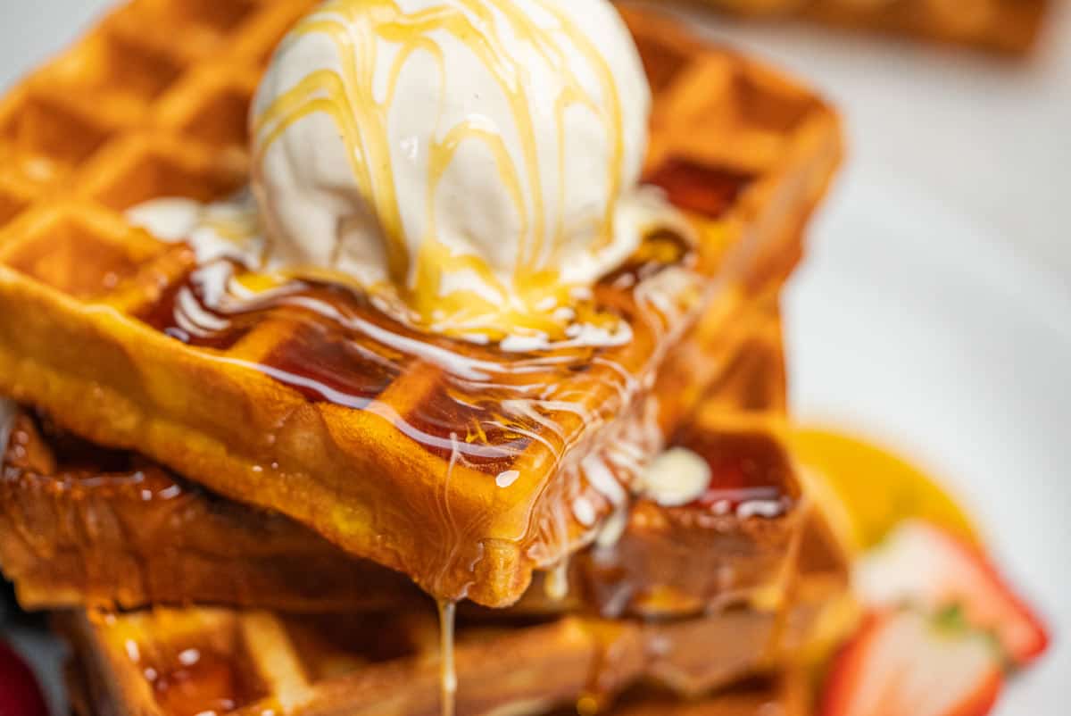 Close-up shot of stacked waffles topped with a melting scoop of vanilla ice cream and drizzled with syrup.